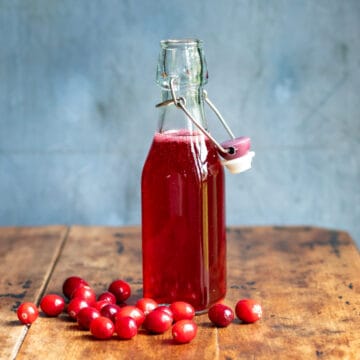 Bottle of cranberry syrup on a wooden table next to fresh cranberries.