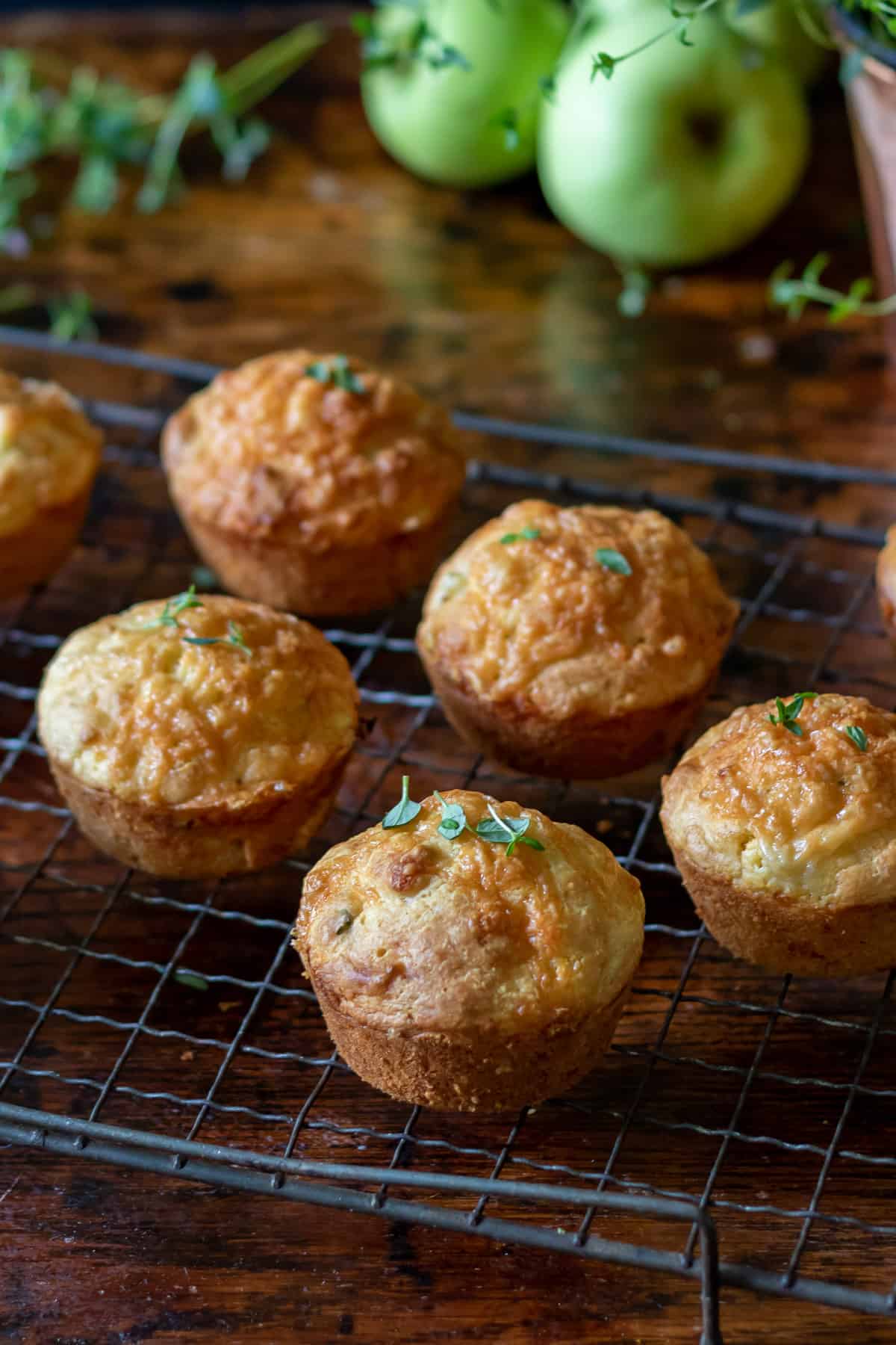 Apple cheddar cheese muffins topped with sprigs of thyme on a wire rack on a wooden table.