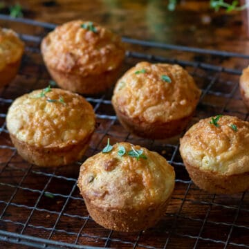 Apple cheddar cheese muffins topped with sprigs of thyme on a wire rack on a wooden table.