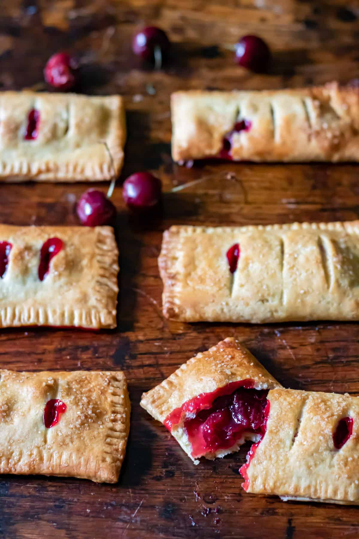 Rows of cherry hand pies on a table, and one is broken in two.