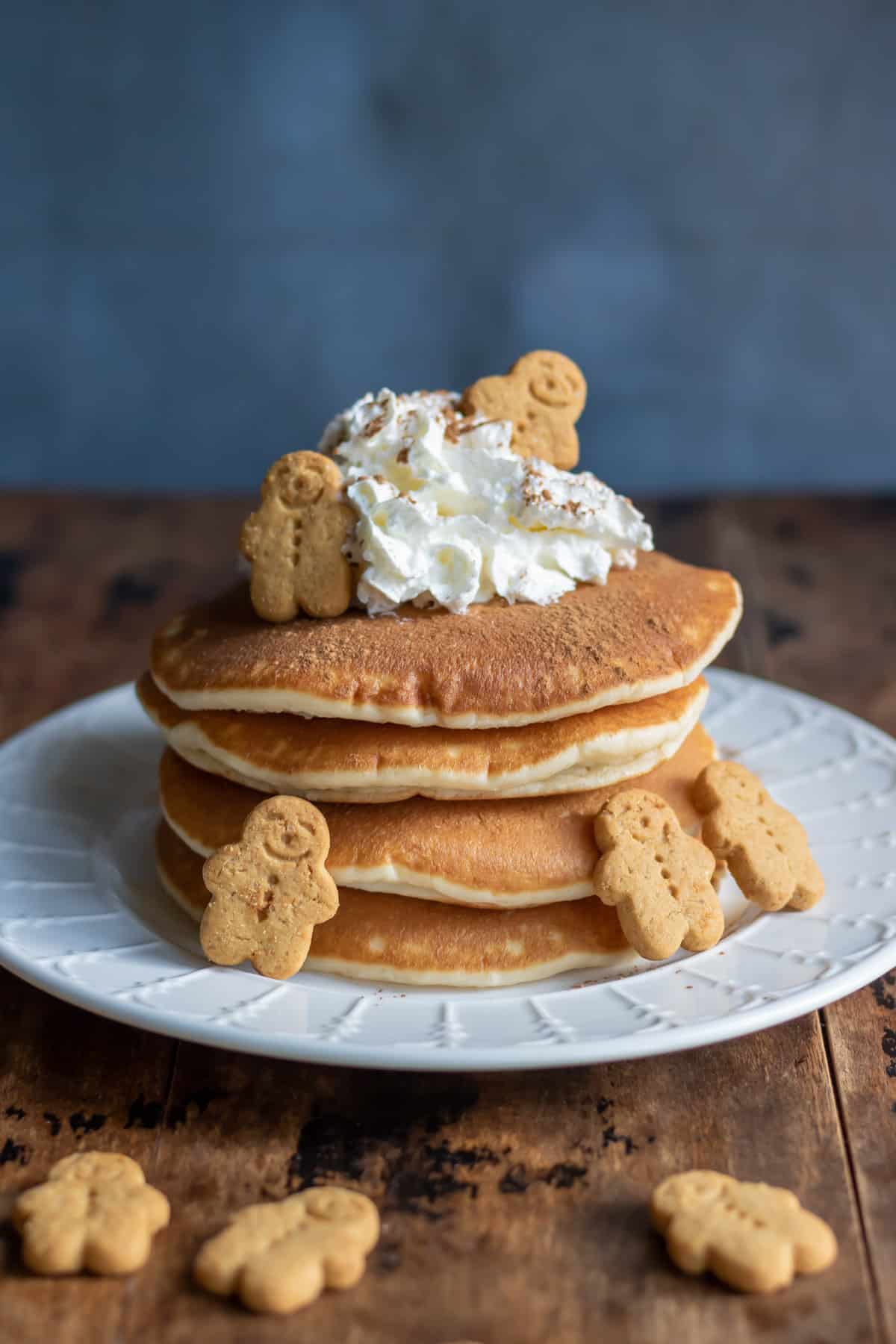 A wooden table with a plate of gingerbread pancakes topped with cream and scattered with mini gingerbread men.