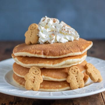 Stack of gingerbread pancakes topped with whipped cream and gingerbread men.