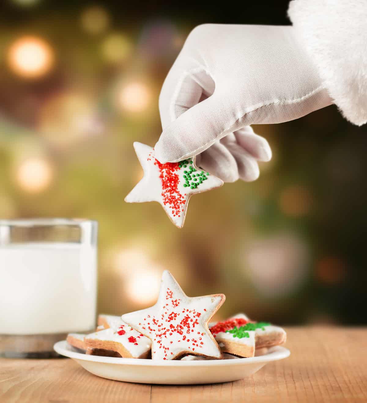 Santa taking a star shaped cookie, in front of a glass of milk and a Christmas tree.