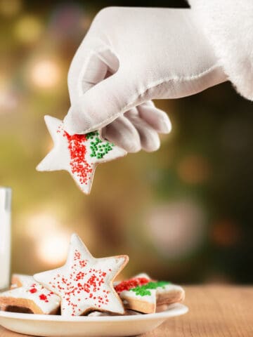 Santa taking a star shaped Christmas cookie, next to a glass of milk.