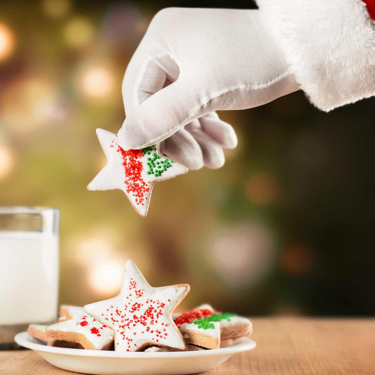 Santa taking a star shaped Christmas cookie, next to a glass of milk.