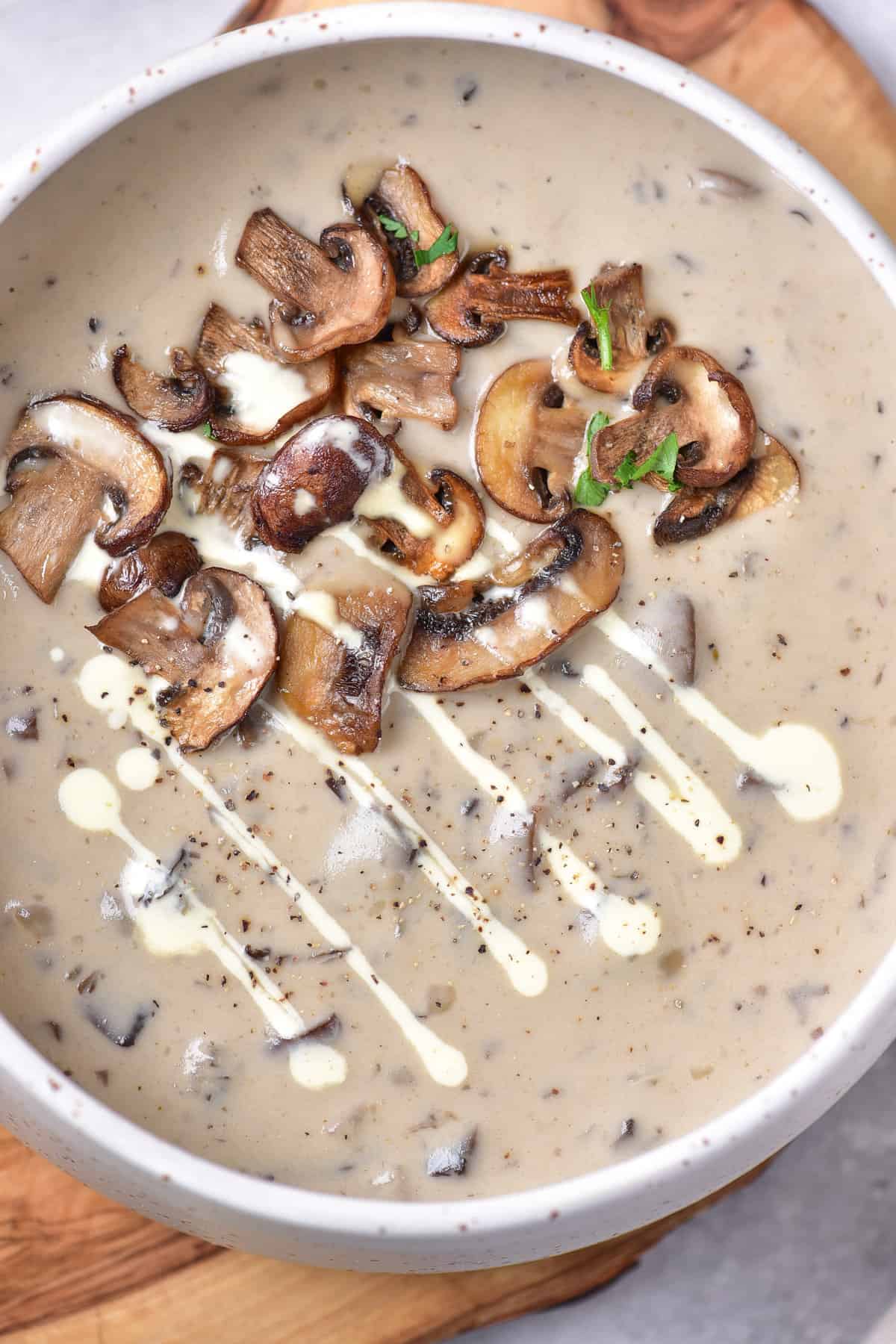 Close up of a bowl of mushroom soup, drizzled with cream and topped with fried mushrooms.