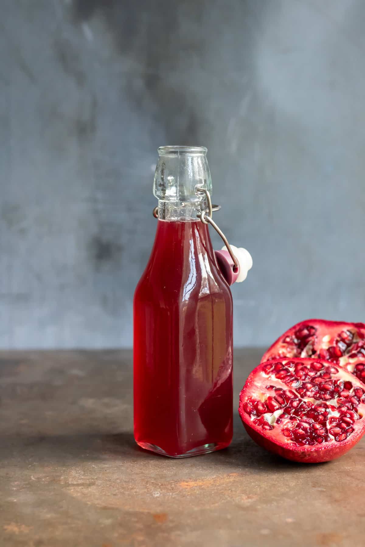 Fresh pomegranate and bottle of pomegranate simple syrup on a table.