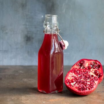 Bottle of pomegranate syrup on a wooden table next to a cut open pomegranate.