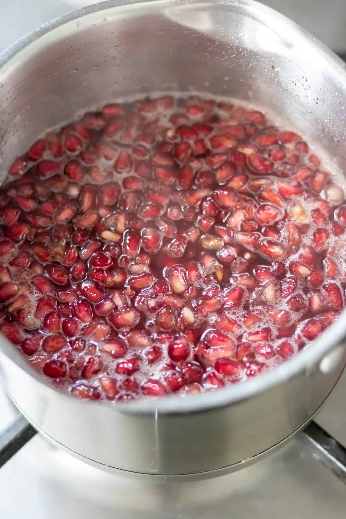 Simmering the pomegranate seeds, sugar and water in a pot to make the syrup.