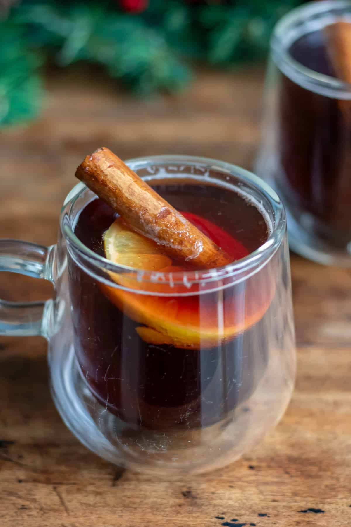 Close up of a mug of hot mulled beer with a cinnamon stick and slice of lemon in it.