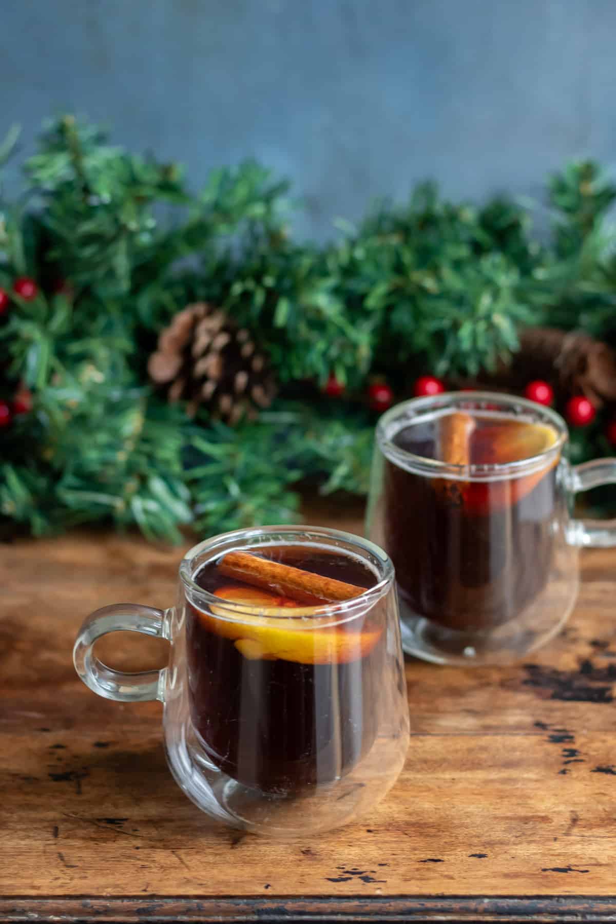 Mugs of gluhbier (hot mulled beer) on a wooden table, with cinnamon sticks and lemon slices.