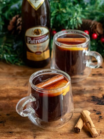 Two mugs of hot mulled gluhbeir on a wooden table, in front of a bottle of beer.