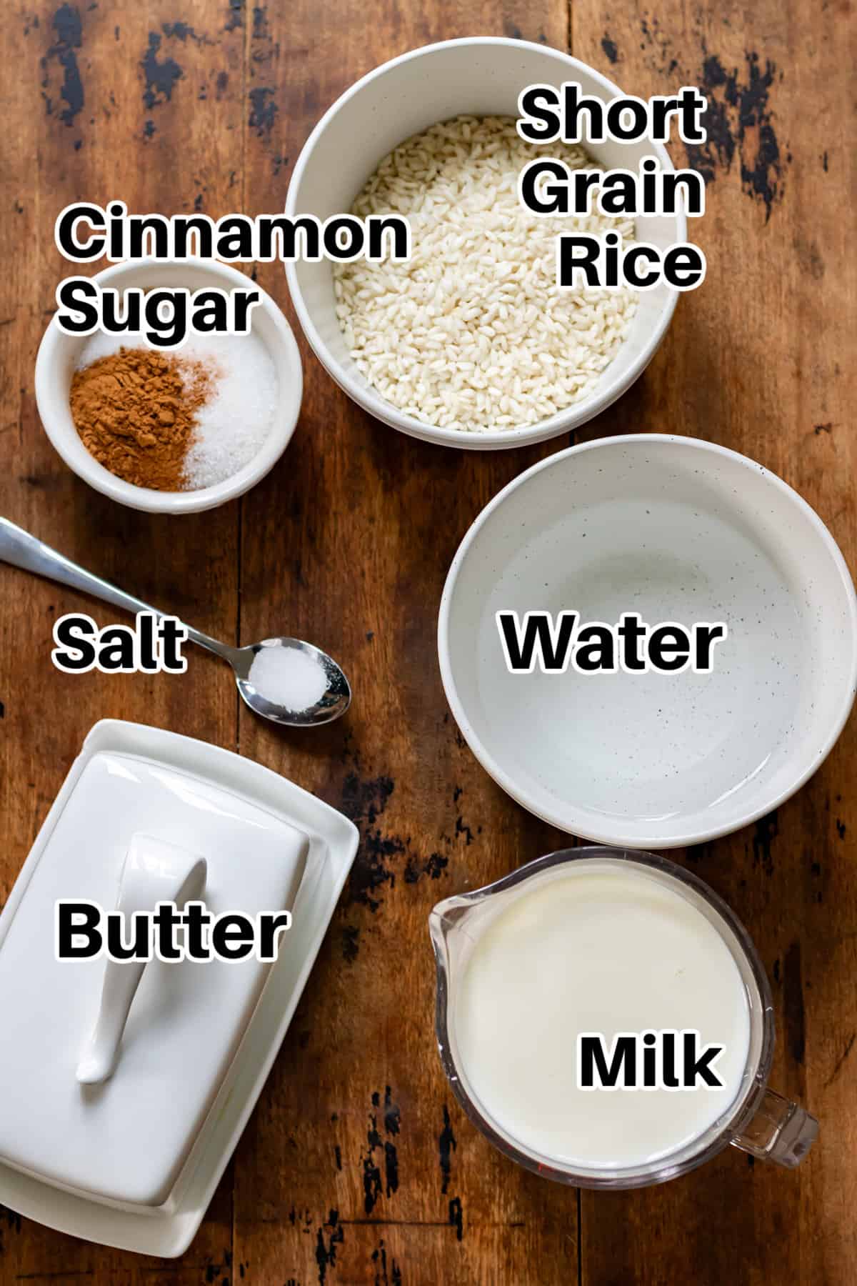 Short grain rice, cinnamon, sugar, water, salt, butter and milk on a table.