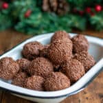 Dish of rumkugeln rum balls on a wooden table in front of a Christmas pine garland.