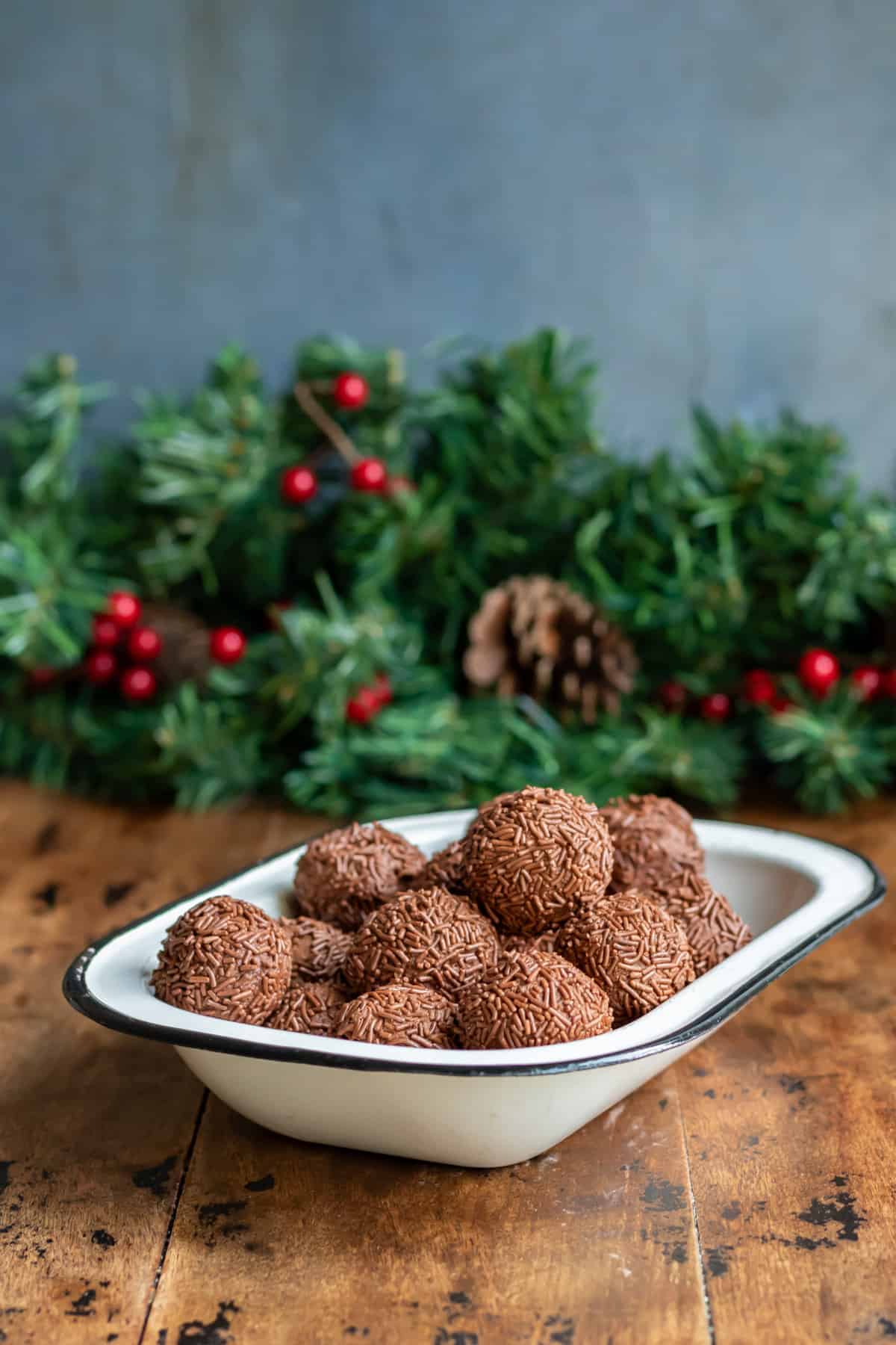 Dish of rumkugeln rum balls on a wooden table in front of a Christmas pine garland.