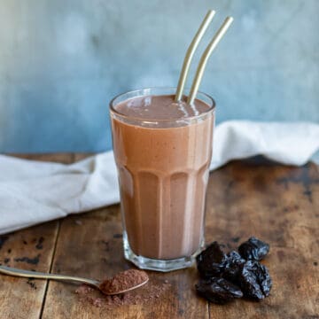 A chocolate prune smoothie in a glass on a wooden table.