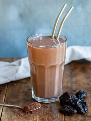 A chocolate prune smoothie in a glass on a wooden table.