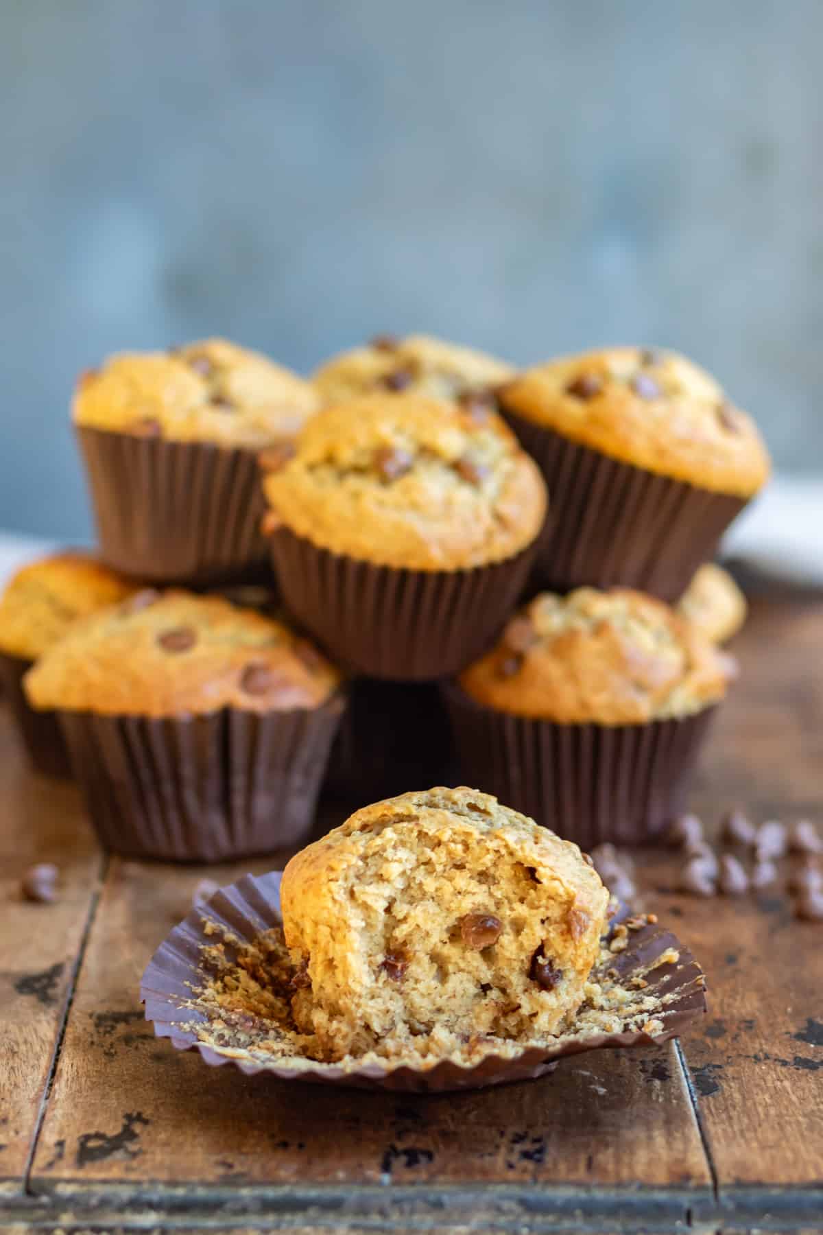 A peanut butter chocolate chip muffin with a bite out, in front of a pile of muffins.