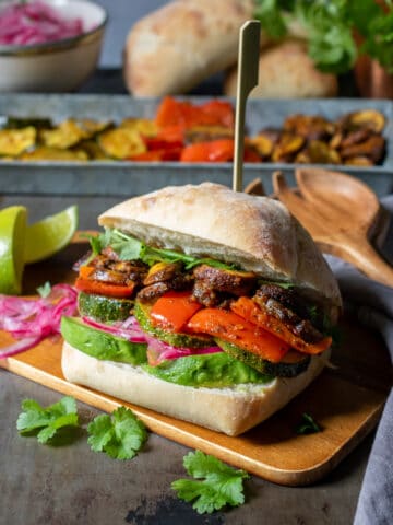 Table with a vegetable Peruvian sandwich on a wooden board in front of dishes of ingredients.