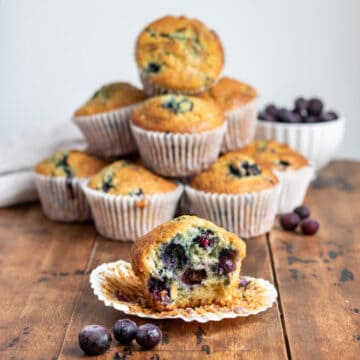A table with a pile of buttermilk blueberry muffins, with one with a bite out in the front.