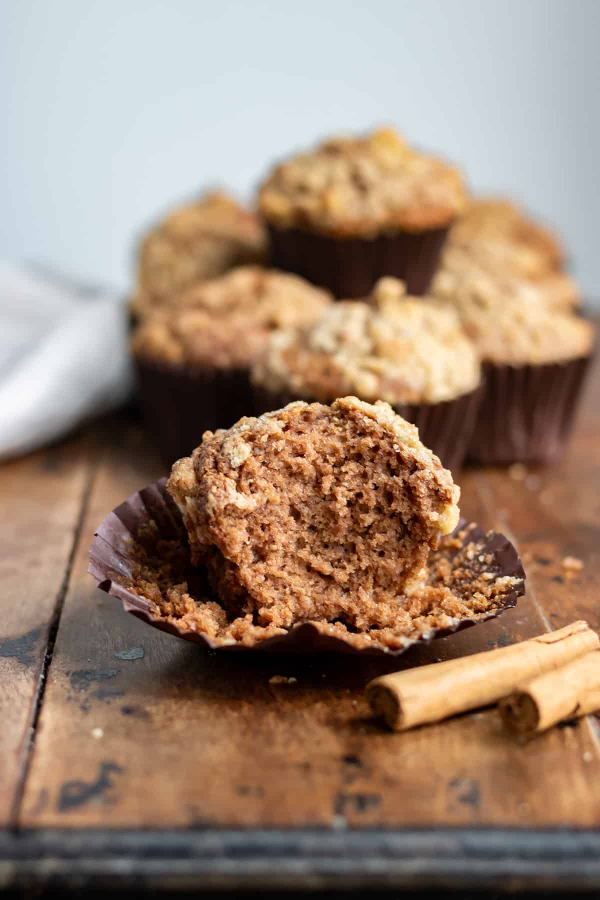 A wooden table with a cinnamon muffin with a bite out of it.