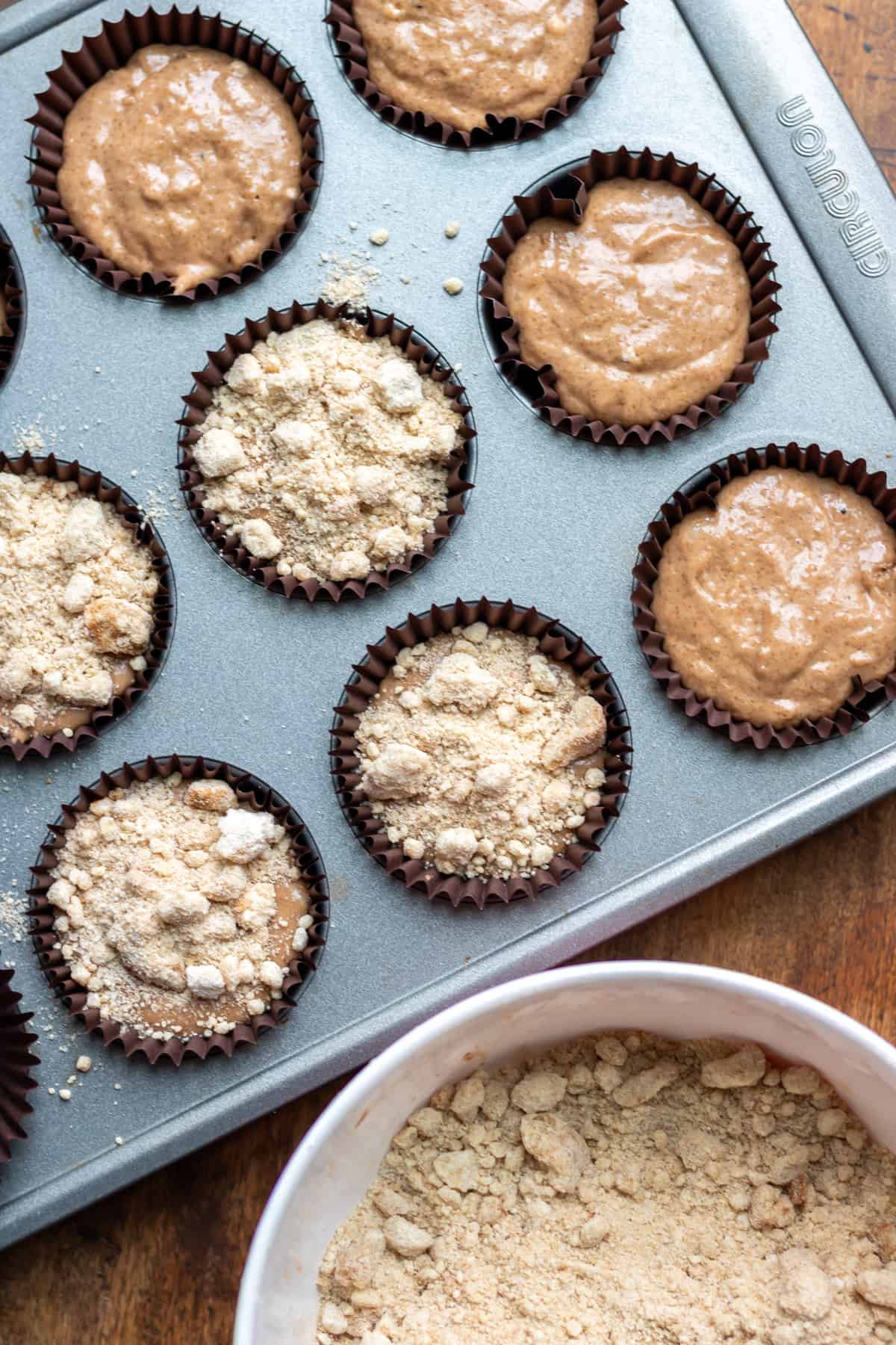 Adding the streusel toppings to the muffin tray with uncooked batter.