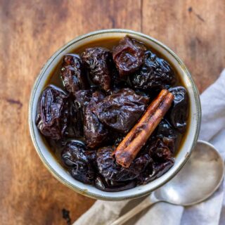 Looking down at a dish of prune compote with a spoon on a wooden table.