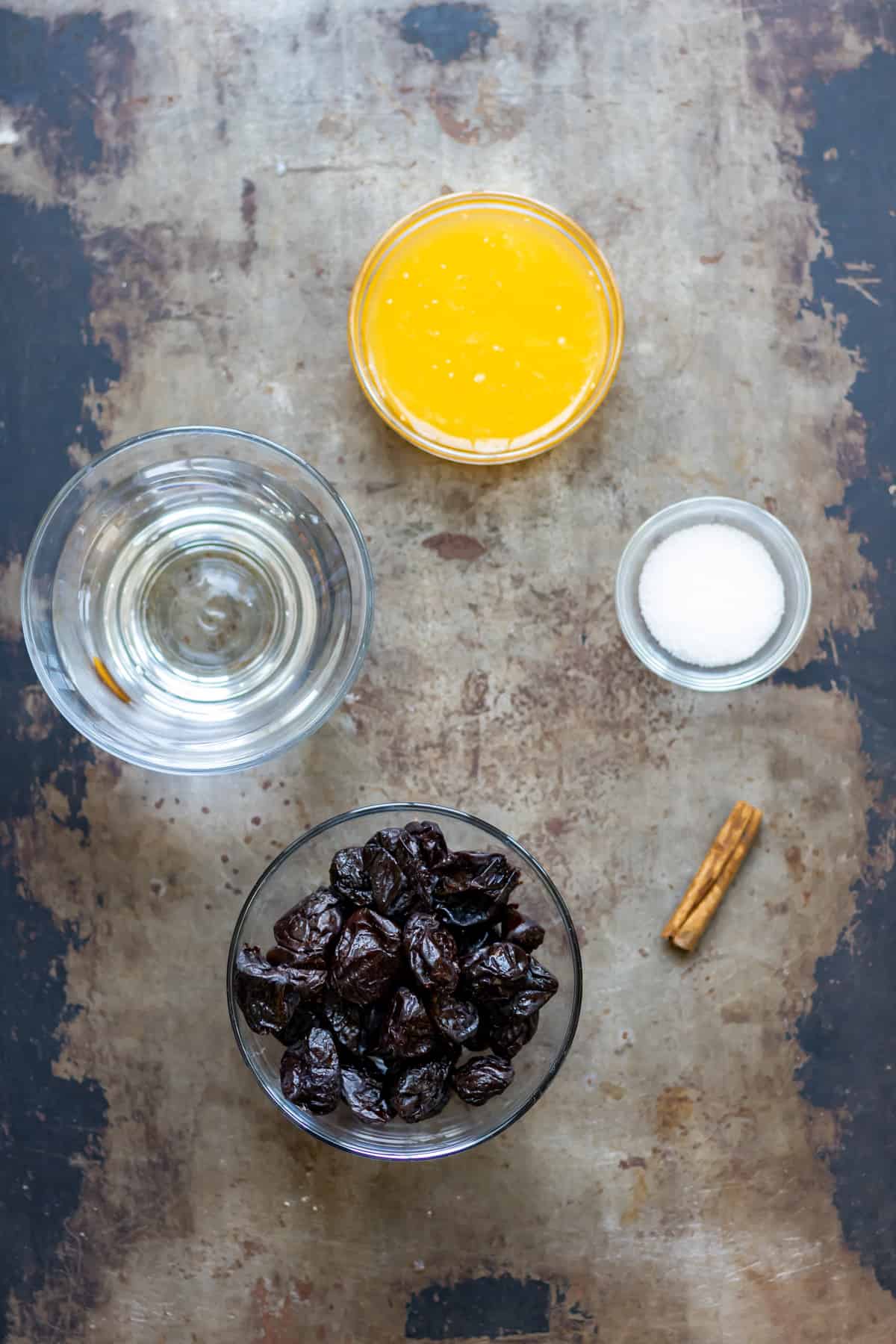 Prunes, water, orange juice, sugar and cinnamon on a table.