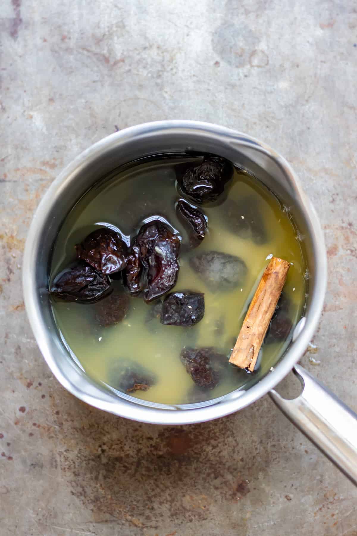 Prunes in a pot with water, sugar, orange juice and a cinnamon stick.