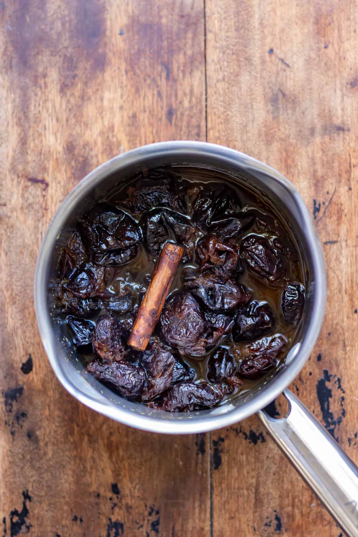 Pot of cooked prune compote with a cinnamon stick.