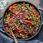 Serving dish of Asian Coleslaw on a table next to a dish of sesame seeds.