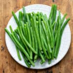 A wooden table with a plate of blanch green beans.