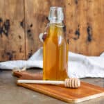 Table with a glass bottle of honey syrup, with a wooden honey spoon next to it.