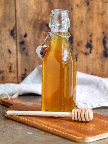 Table with a glass bottle of honey syrup, with a wooden honey spoon next to it.