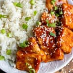 A plate of rice and Korean tofu in a thick sticky sauce, with sesame seeds and sliced scallions.