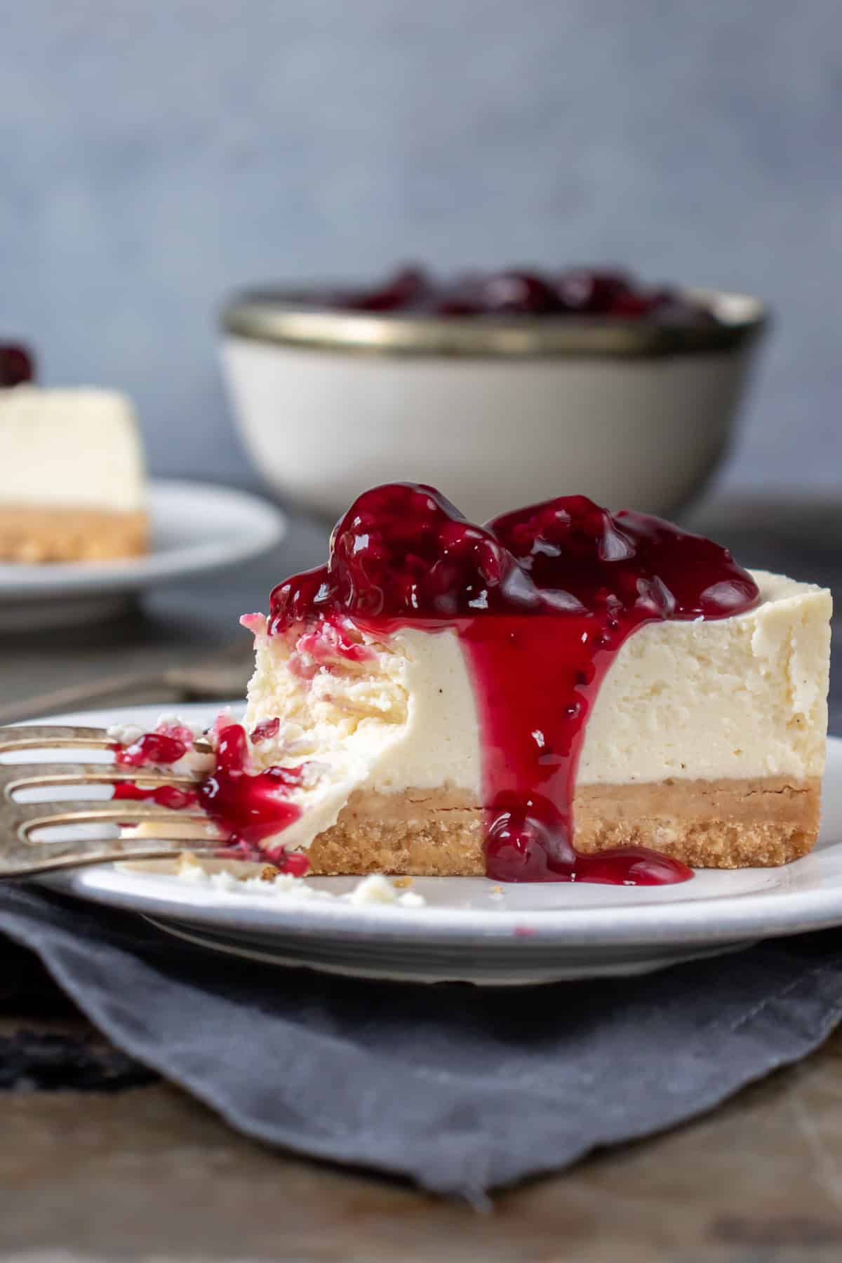 Close up of a fork taking a bite out of a slice of cheesecake.