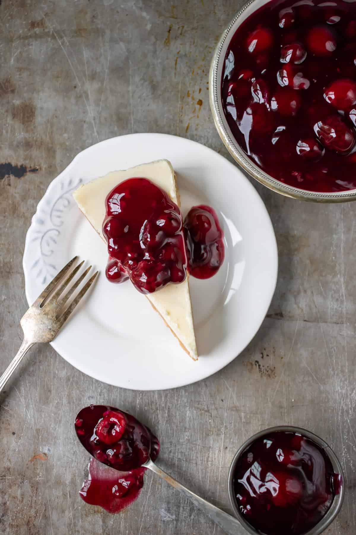 Looking down at a table with a plate of vegan cheesecake next to dishes of berry sauce.