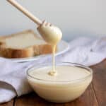 A wooden honey stick coming out of a dish of whipped honey.