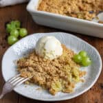 Table with a plate of gooseberry crumble, topped with a scoop of vanilla ice cream.