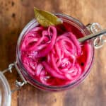 Looking down at a jar of pickled red onion with a fork in it and a bay leaf.