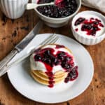 Table with a plate of pancakes, and a dish of yogurt, each topped with blackcurrant compote.