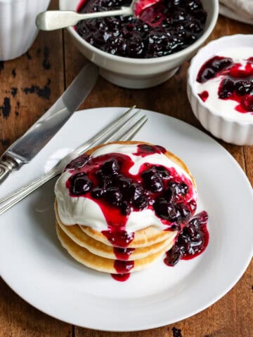 Table with a plate of pancakes, and a dish of yogurt, each topped with blackcurrant compote.