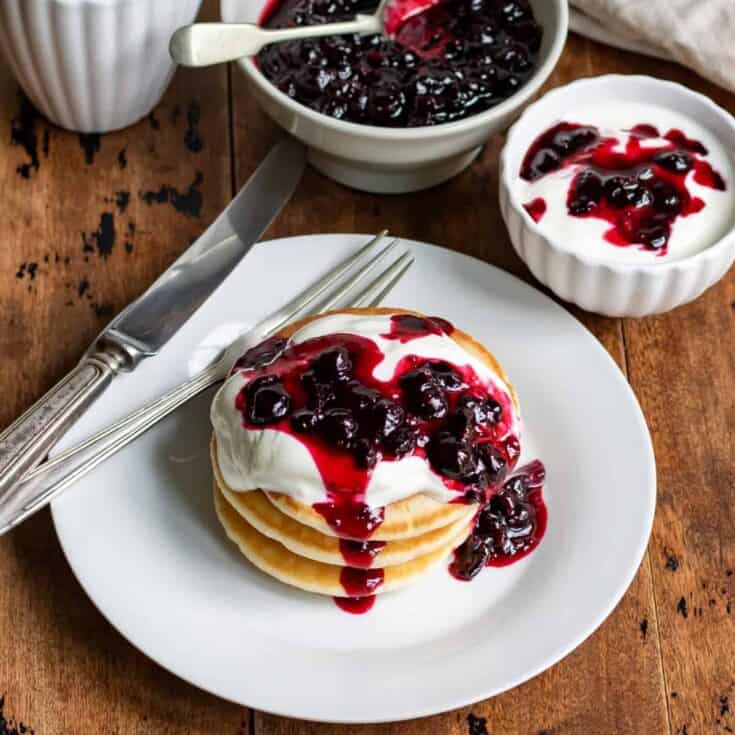 Table with a plate of pancakes, and a dish of yogurt, each topped with blackcurrant compote.