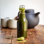 Wooden table with a spoon of matcha powder, bottle of matcha syrup and in the background a teapot and Japanese cups.