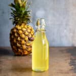 Glass bottle of pineapple simple syrup in front of a pineapple.