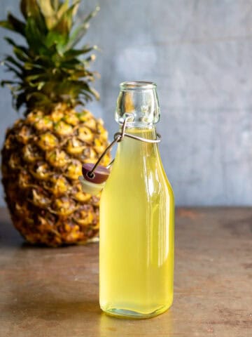 Glass bottle of pineapple simple syrup in front of a pineapple.