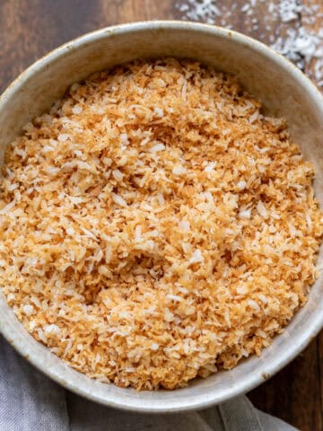 Bowl of toasted shredded coconut on a wooden table.