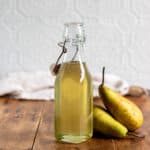 Wooden table with a bottle of pear syrup and two pears next to it.
