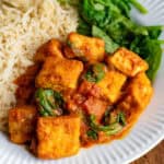 Close up of tofu curry on a plate with rice and wilted spinach.