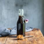 Wooden table with a glass bottle of brown sugar syrup with a teaspoon of brown sugar in front of it.